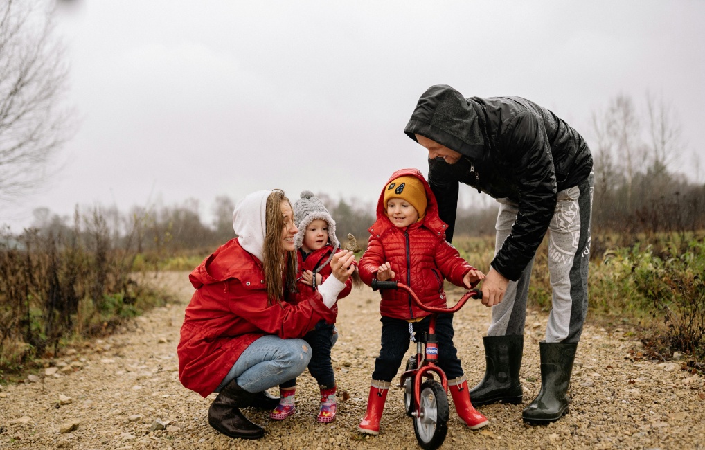 Family with two young kids riding their bikes on a woodland path