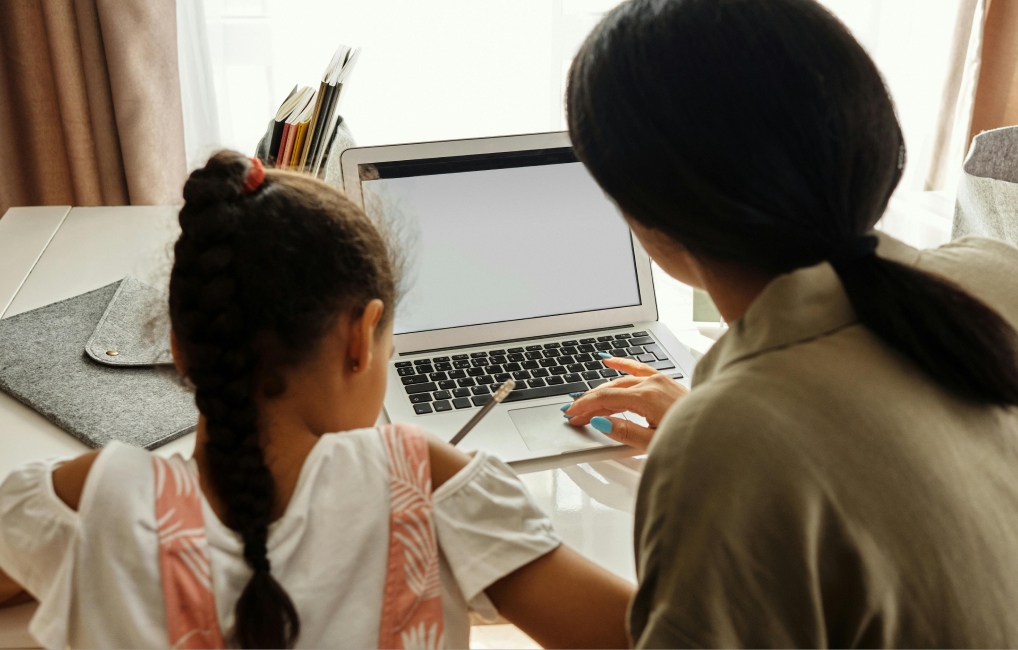 Mother teaching daughter sitting at a laptop