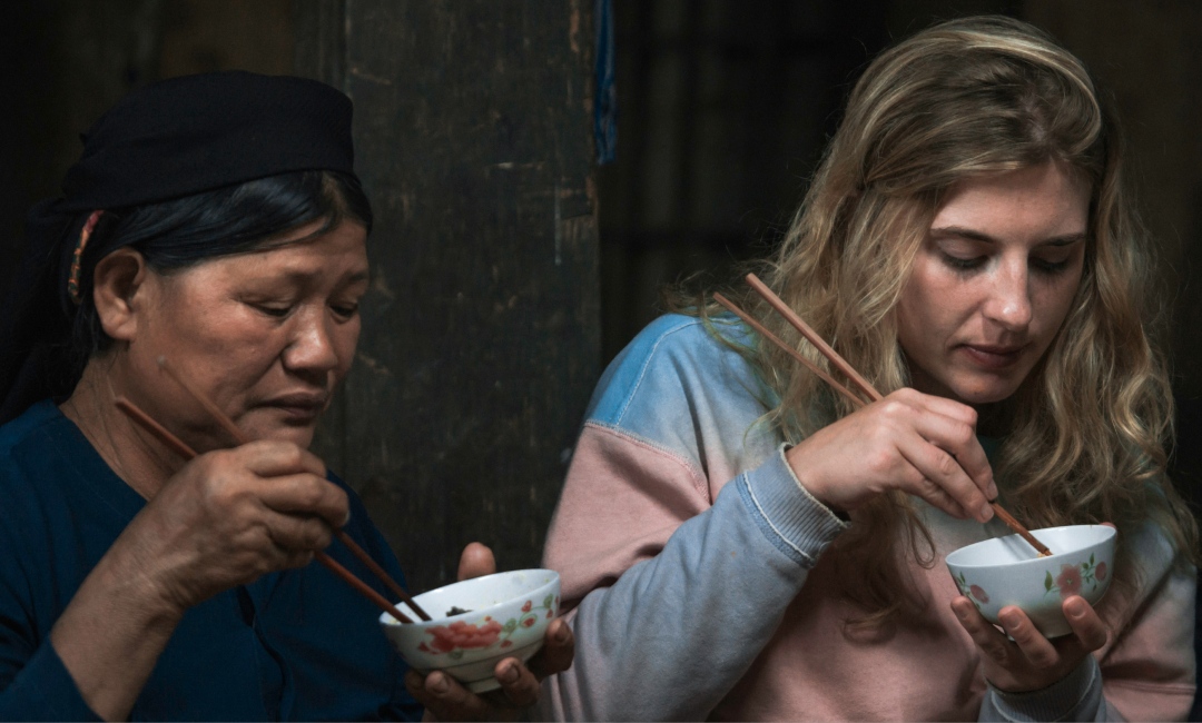 Two women eating a cultural dish with chopsticks