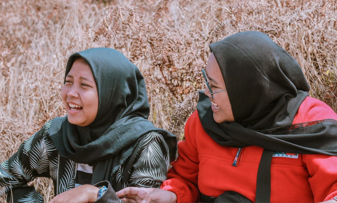 Two women laughing while sitting in some tall grass
